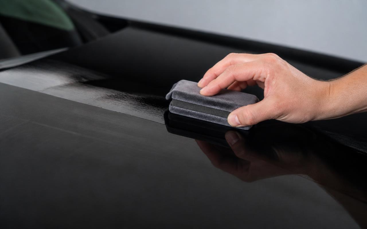 Hand spreading ceramic coating on black car paint with a suede applicator block