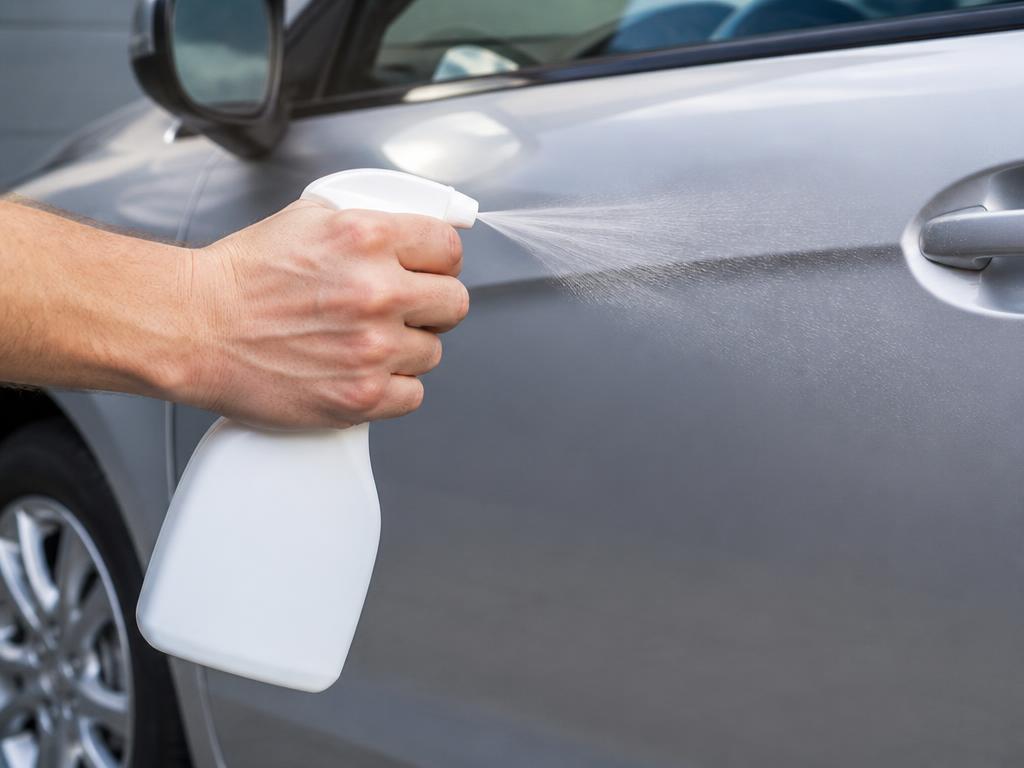 Hand gripping an unlabeled spray bottle and misting an eco-friendly cleaner onto a car door panel