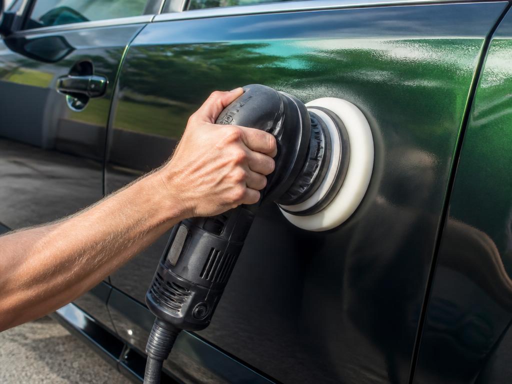 Hand gripping a dual-action polisher pressed against a glossy dark green car door during paint correction