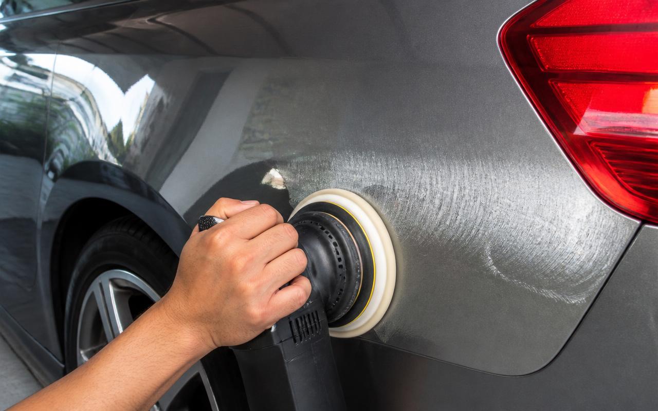 Hand correcting swirl marks on a grey car fender with a dual-action polishing machine
