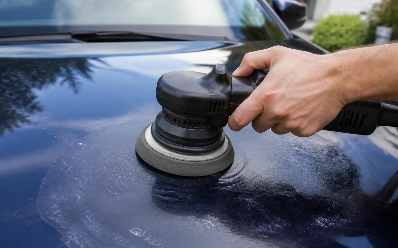 Hand operating a dual-action polisher on a dark blue car hood during paint correction before ceramic coating