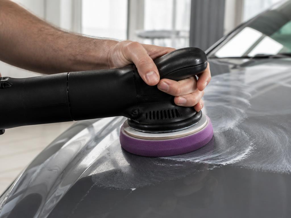 Detailer's hand gripping a dual-action polisher pressed against glossy grey car paint