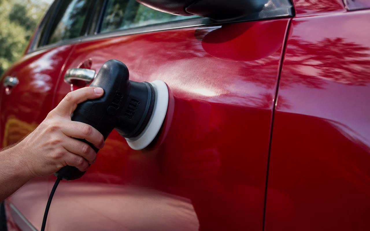 Hand polishing a glossy red car door with a dual-action polisher and foam pad