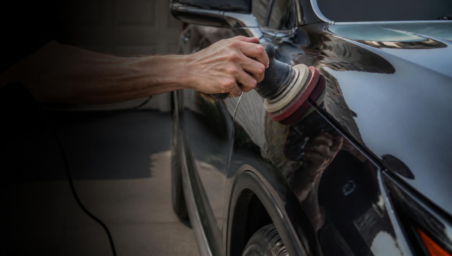 Hand gripping a dual-action polisher against the glossy black fender of a car during a mobile detail